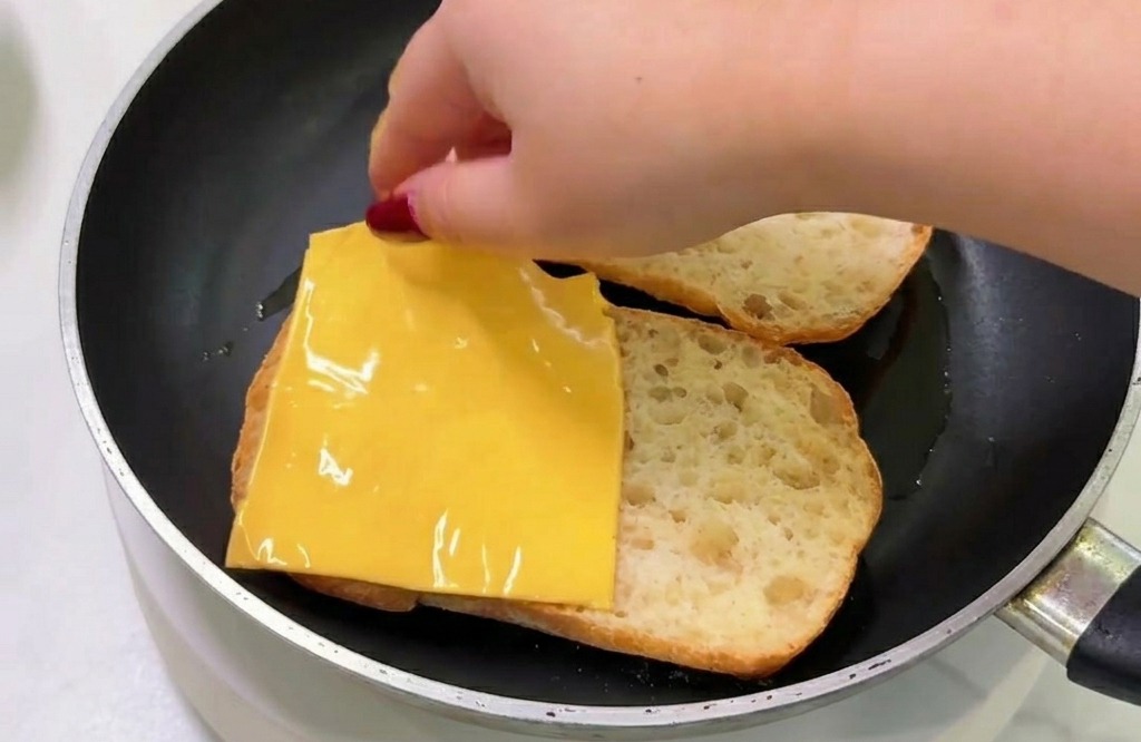 フライパンの中の温かいパンの上に、スライスチーズを乗せている様子。