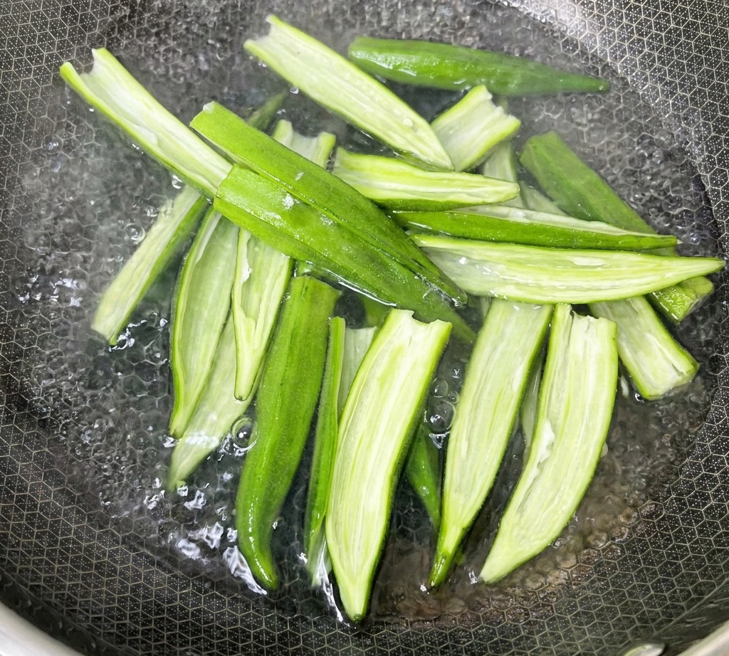 鍋で沸騰したお湯に、種を取り除いたオクラをさっと入れている様子。