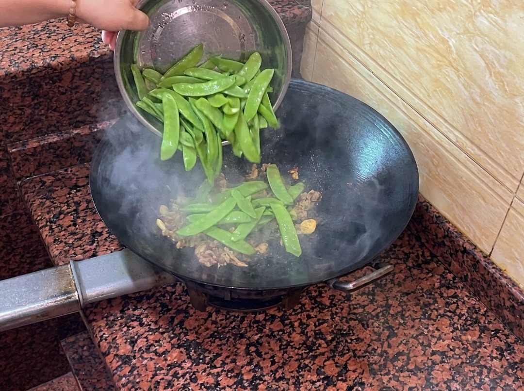 腸詰めと薬味が入った鍋に、新鮮な絹さやが加えられている様子。