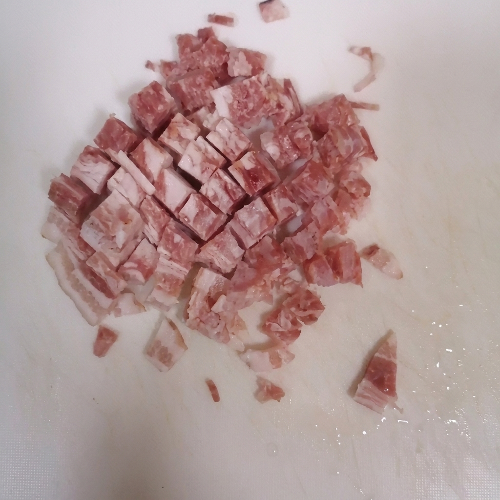 白いまな板の上で小さく角切りにされているベーコン。