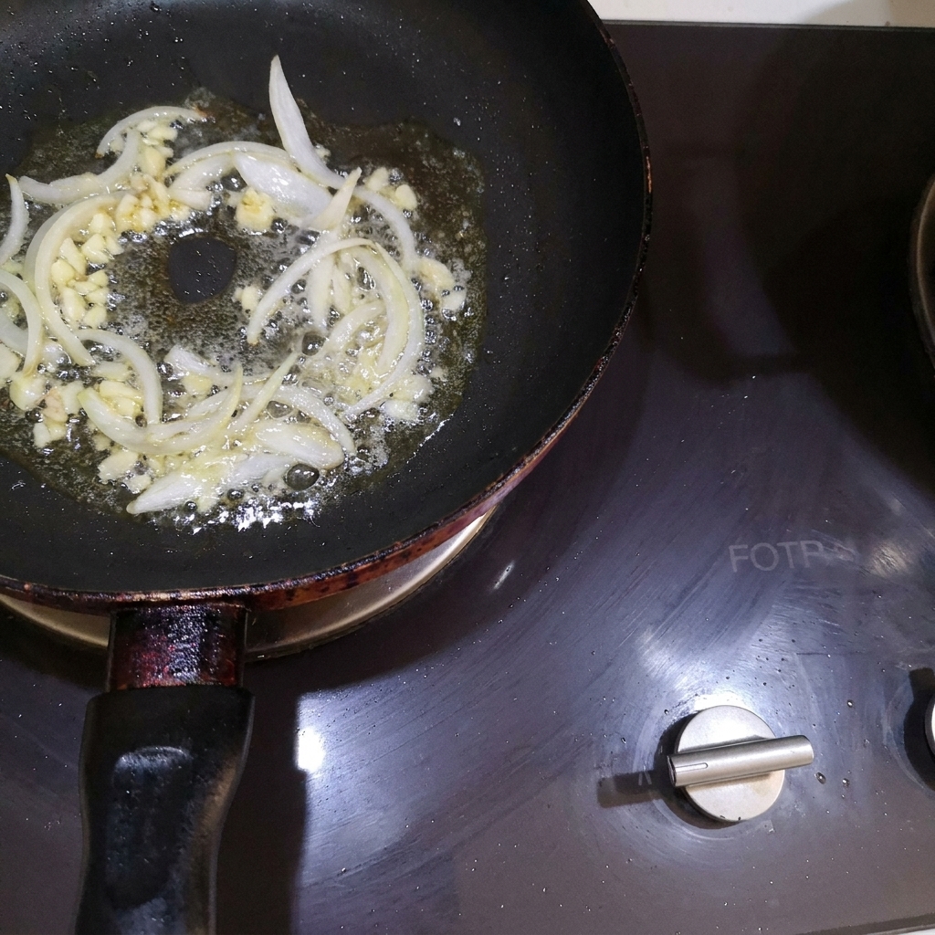 フライパンの溶けたバターにみじん切りの玉ねぎとにんにくを加えて炒めている様子。