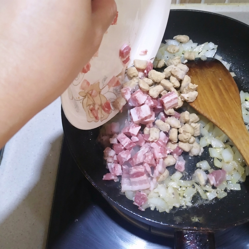 玉ねぎとにんにくと一緒にフライパンで炒められている角切りのベーコンと牛肉。