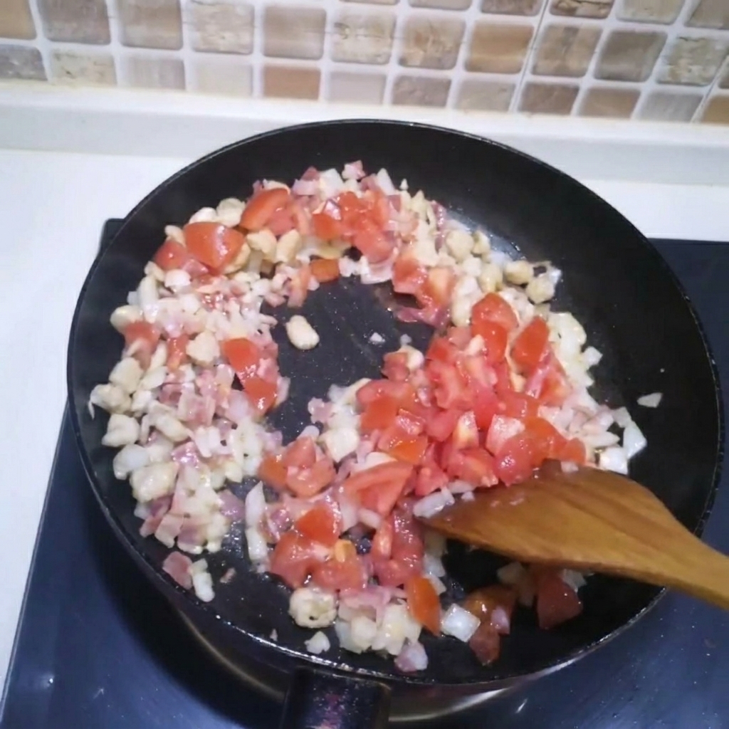 炒めたお肉と玉ねぎのフライパンに角切りのトマトを加えている様子。