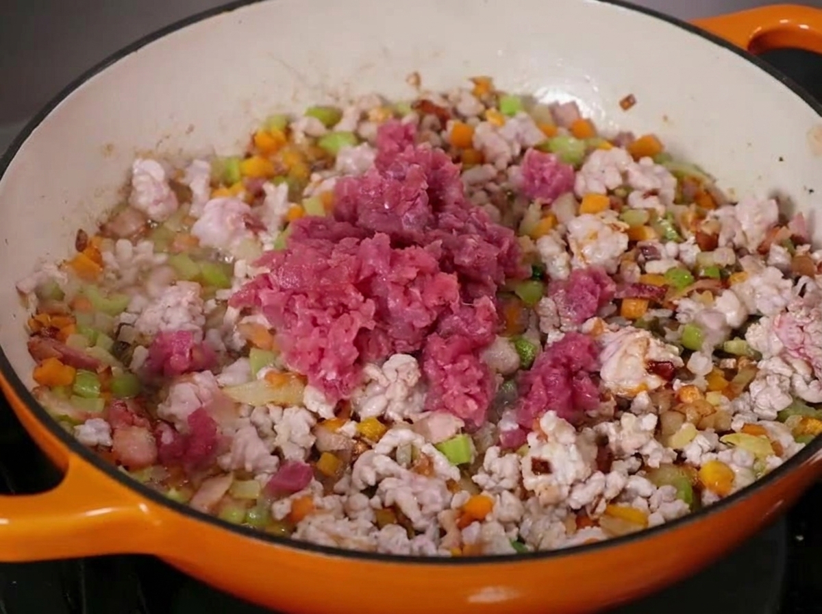 ホーロー製の大きな鋳鉄フライパンで、牛と豚のひき肉を角切り野菜と一緒に炒めている様子。