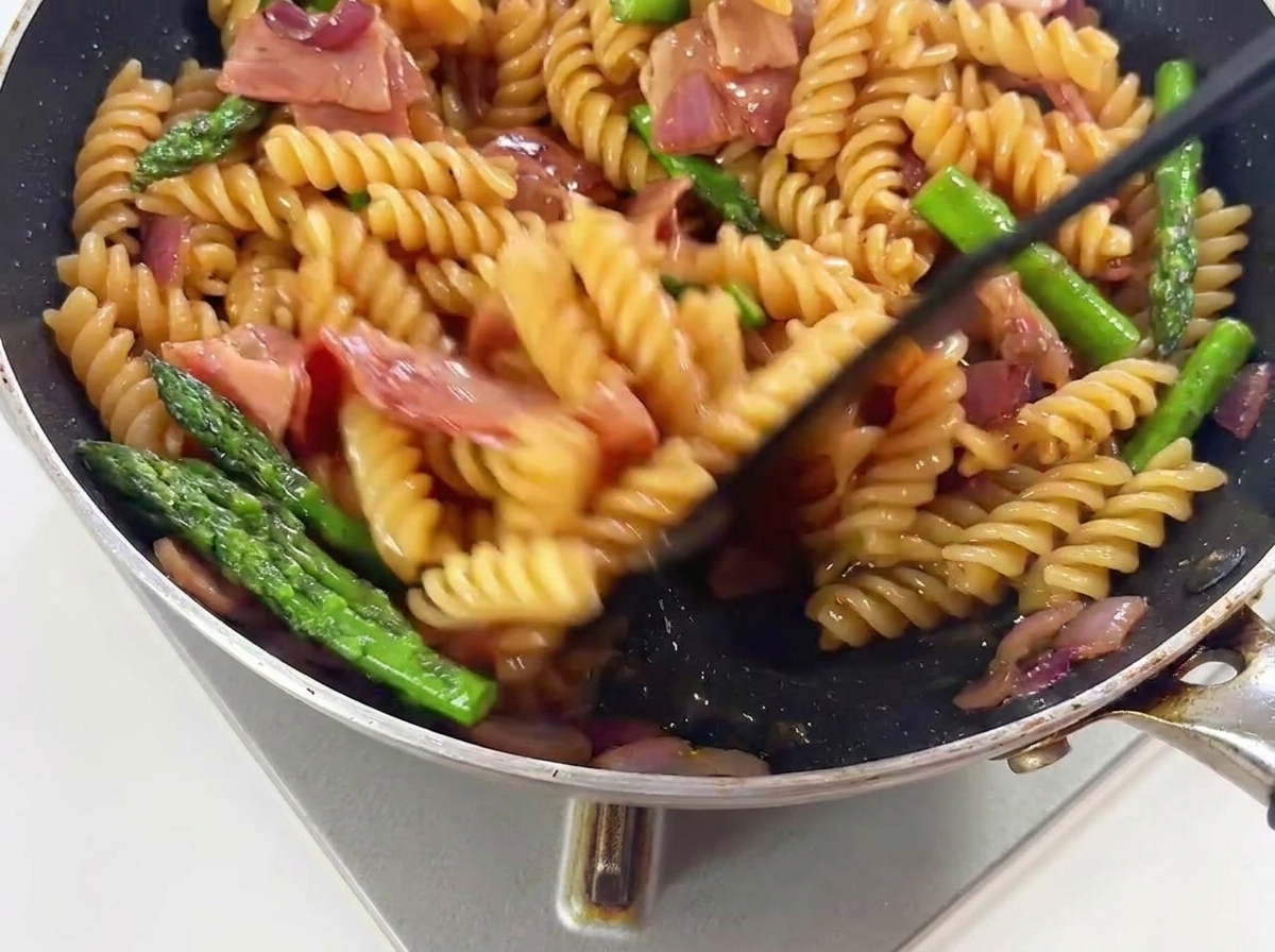 フライパンの中でトングを使ってパスタを盛り付け用に整えている様子。
