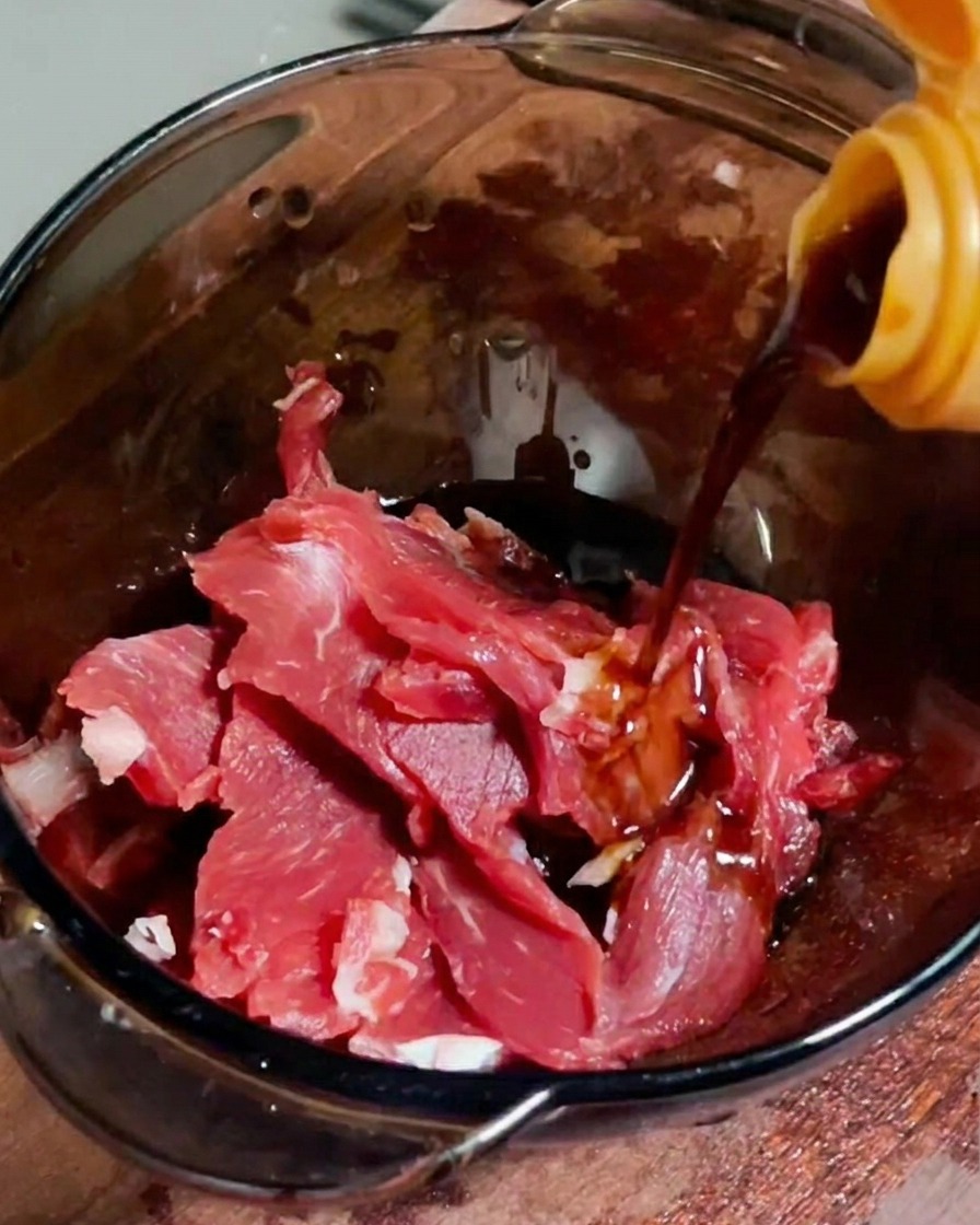 透明なボウルに入った生の牛薄切り肉に醤油を注いでいる様子。