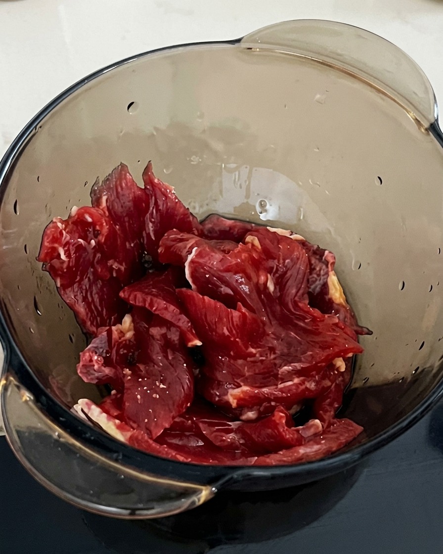 醤油で下味をつけた牛肉に、スプーン一杯の片栗粉を加えている様子。