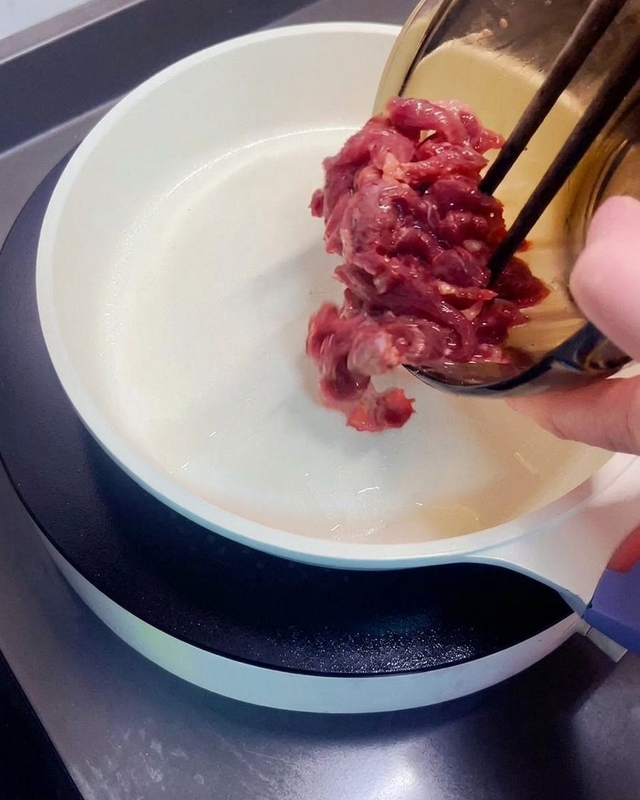 熱したフライパンに下味をつけた牛肉を広げ入れている様子。