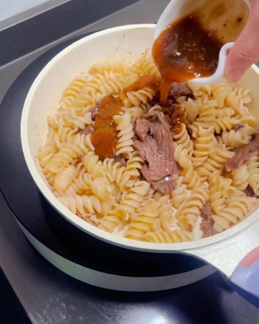 フライパンの牛肉とパスタに、小皿からパスタソースをかけている様子。