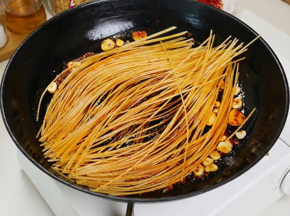 フライパンで焼き付けたスパゲッティに、お玉で赤いトマトスープをかけている様子。