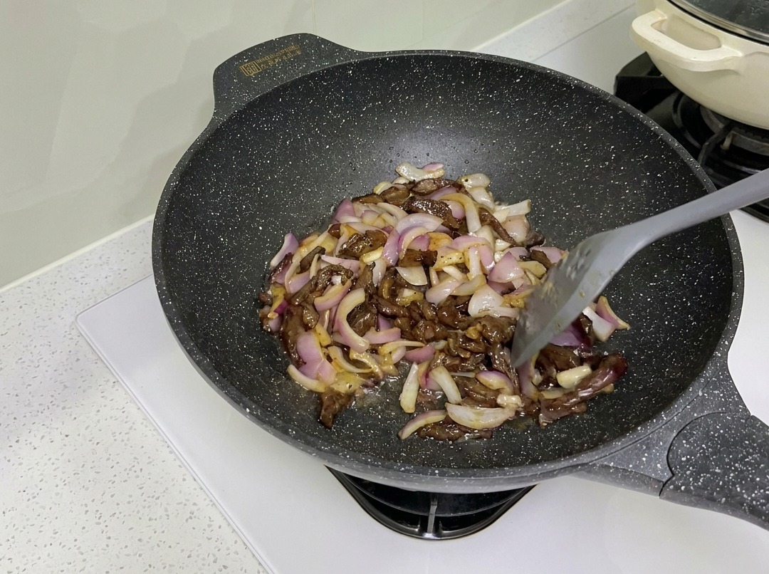 中華鍋で牛肉と赤玉ねぎを炒めている様子。