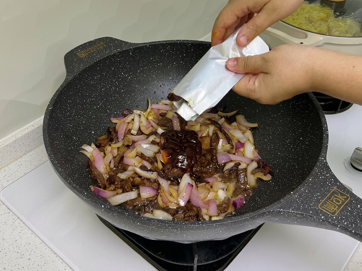調理中の牛肉と玉ねぎにトマトペーストとパスタソースを加えている様子。