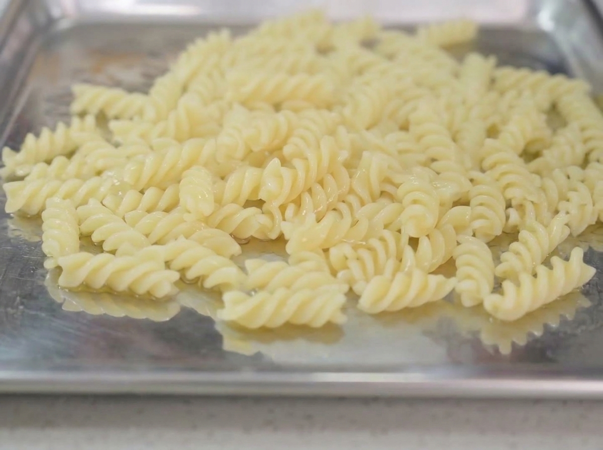 茹で上がったパスタをトレイに広げ、オリーブオイルを回しかけている様子。