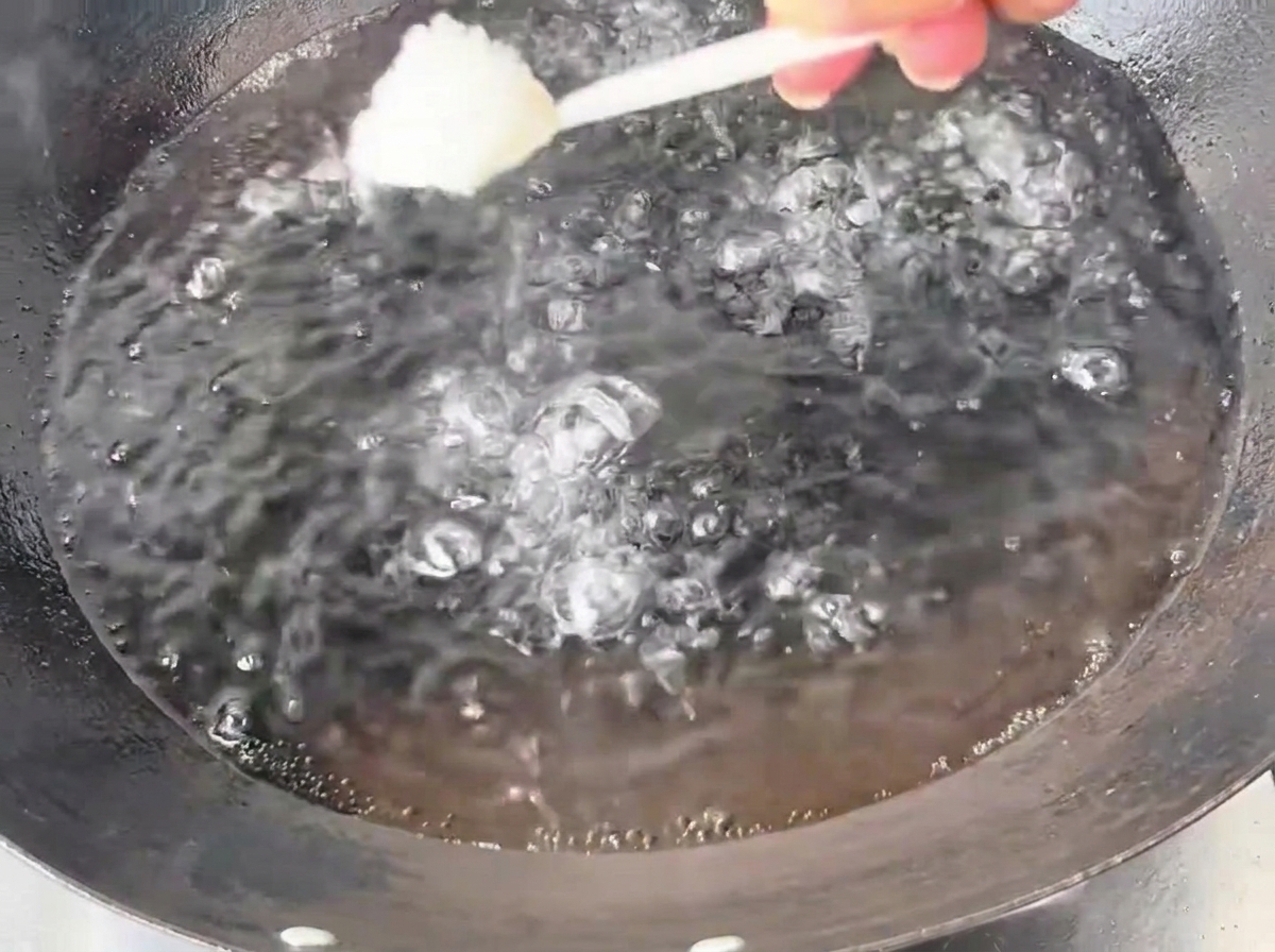グツグツと沸騰した大きなお湯入りの中華鍋に、スプーン一杯の塩を入れている様子。