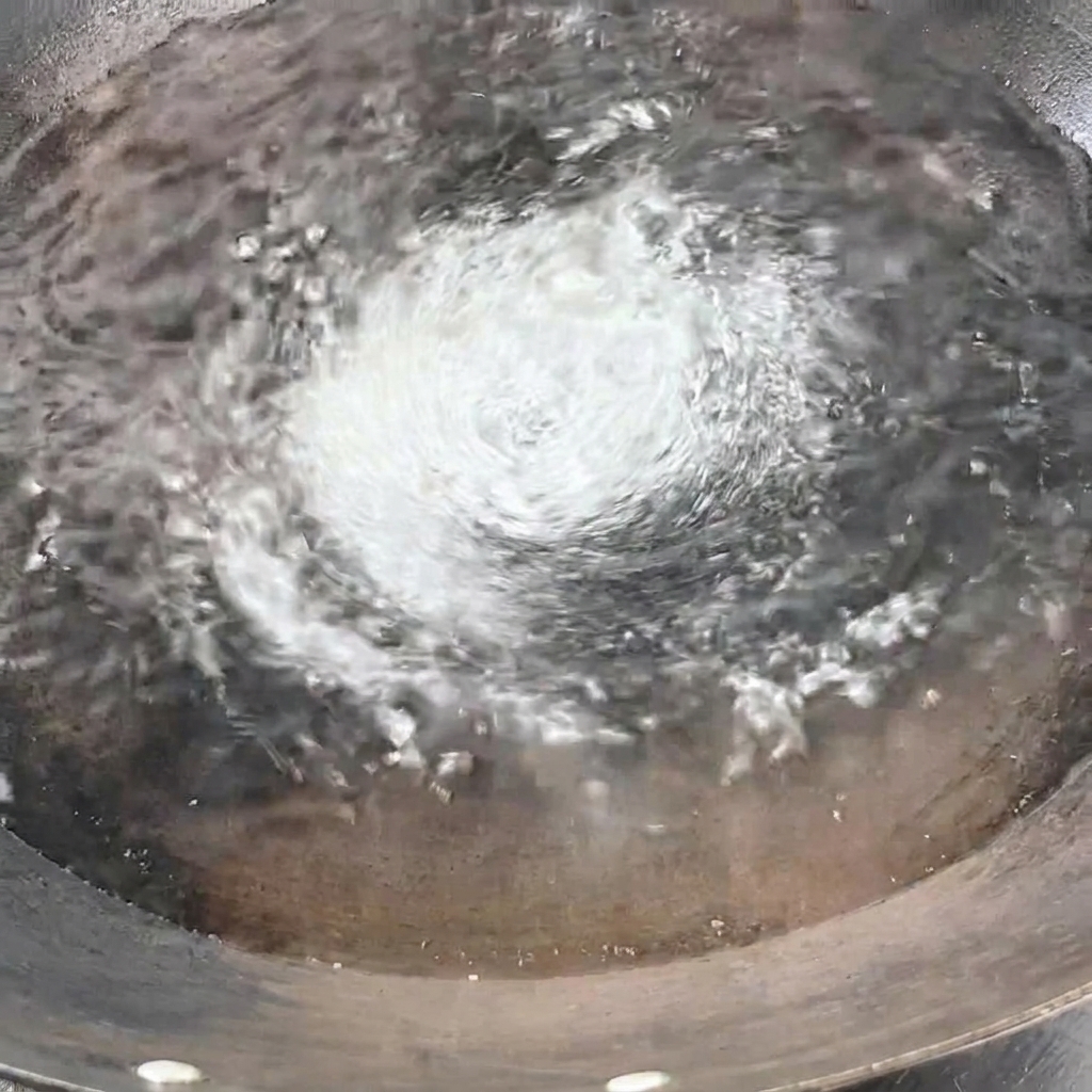 沸騰したお湯の入った鍋に、束になった乾麺のスパゲッティを縦に入れている様子。