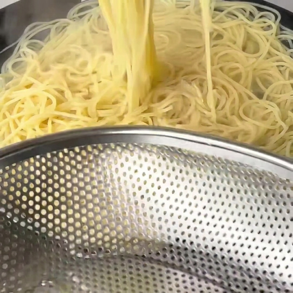 長い菜箸を使って、柔らかく茹で上がったスパゲッティをお湯から引き上げている様子。