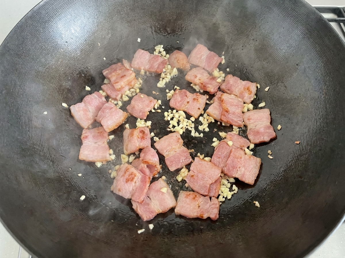 ベーコンとにんにくの入った鍋に、スライスした生のホワイトマッシュルームを入れている様子。