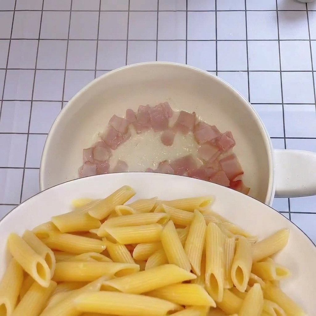 茹で上がったペンネをベーコンの入ったフライパンに移す様子。