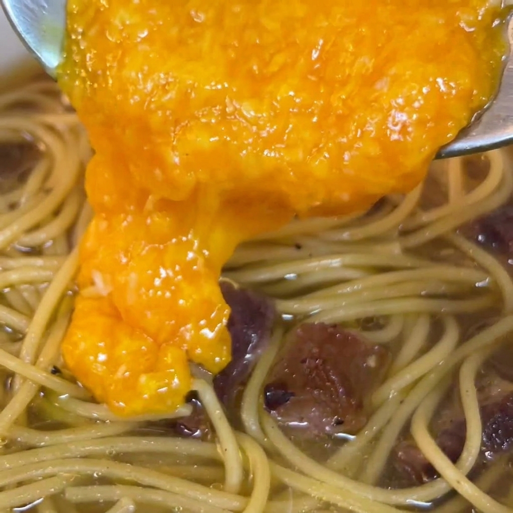 火から下ろしたパスタの上に卵液を注ぐ様子
