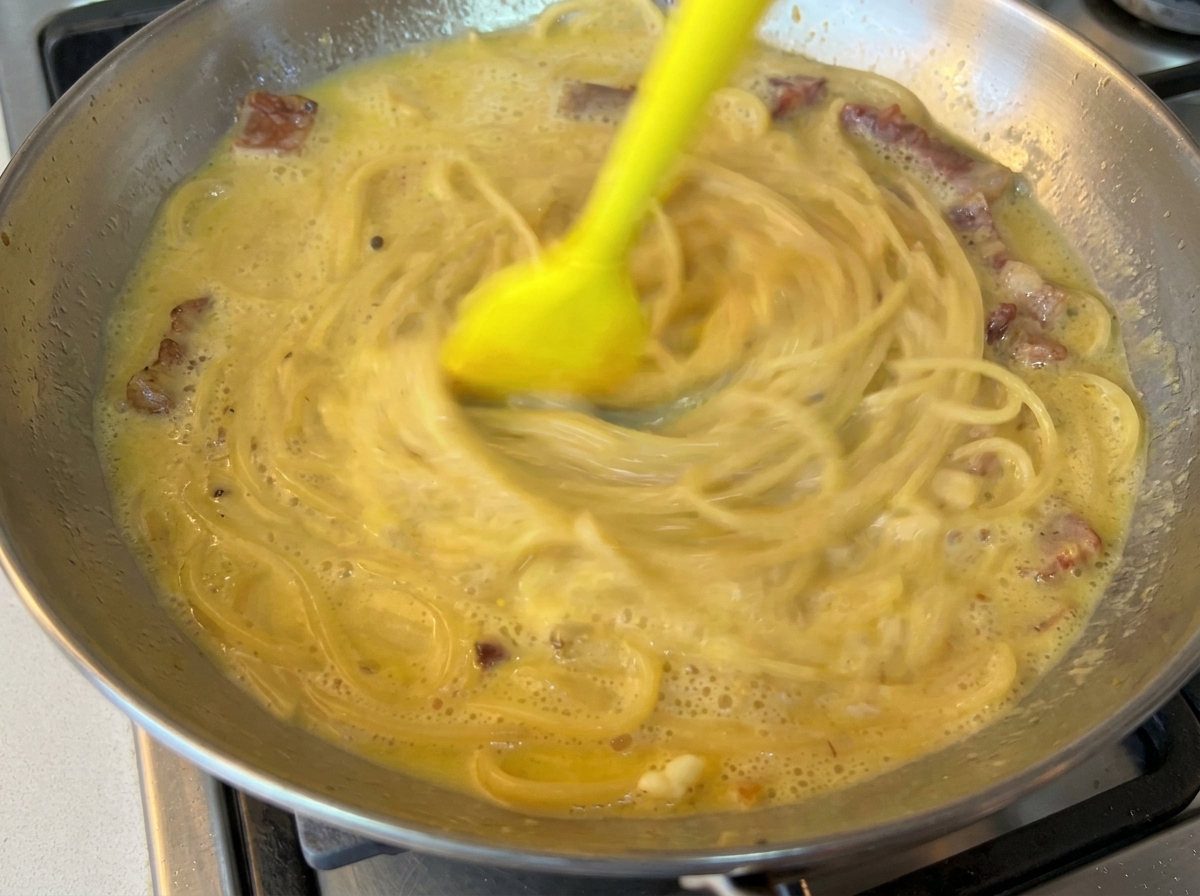 ゴムベラでパスタとソースを素早く混ぜ合わせている様子