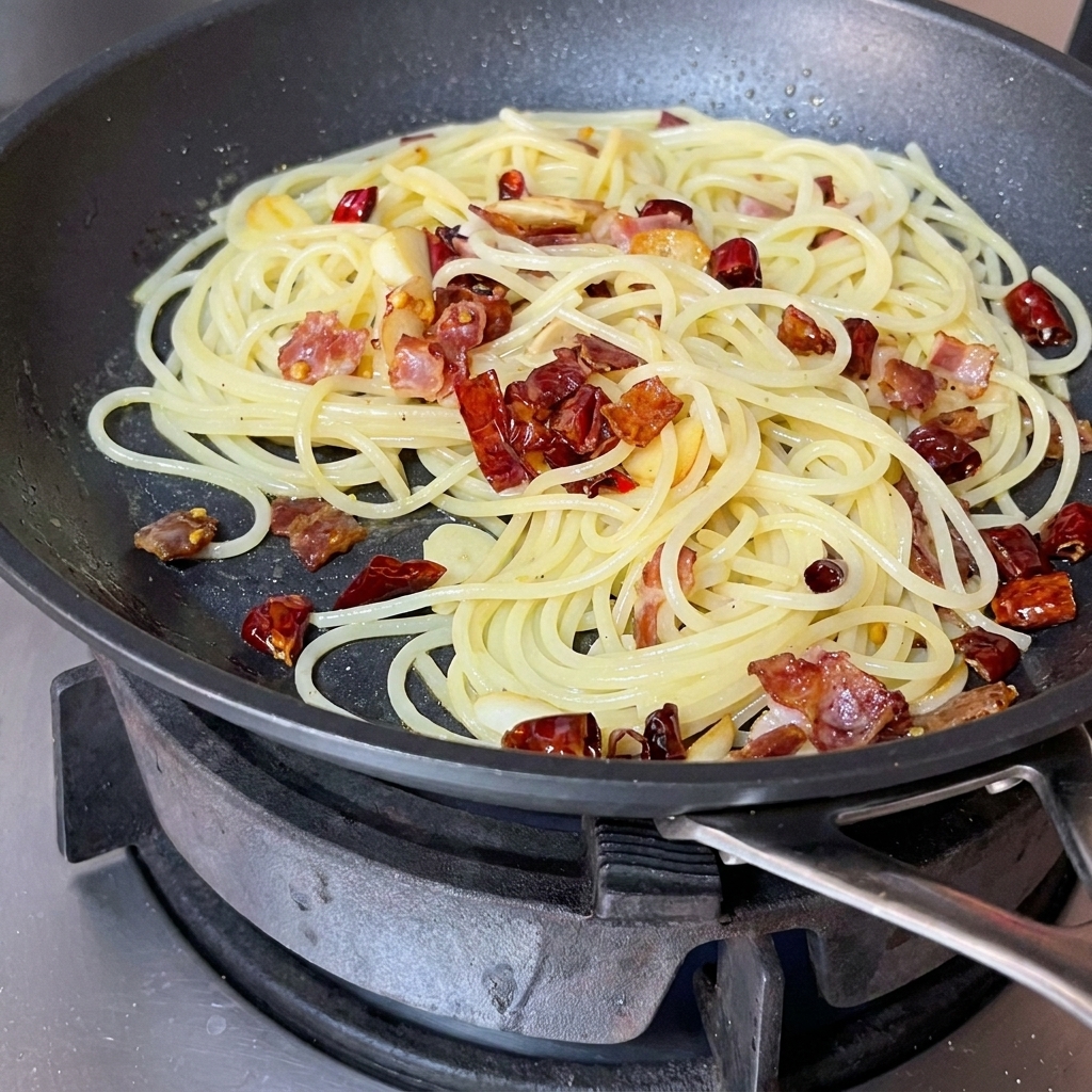 赤いヘラを使って、パスタと具材を勢いよく混ぜている様子。