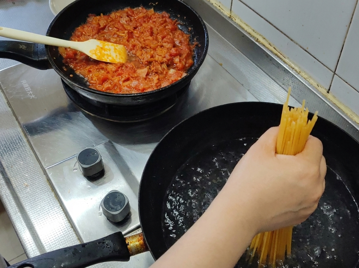 ぐつぐつと沸騰したお湯の入った鍋に、ひとつかみの乾燥スパゲッティを沈める様子。