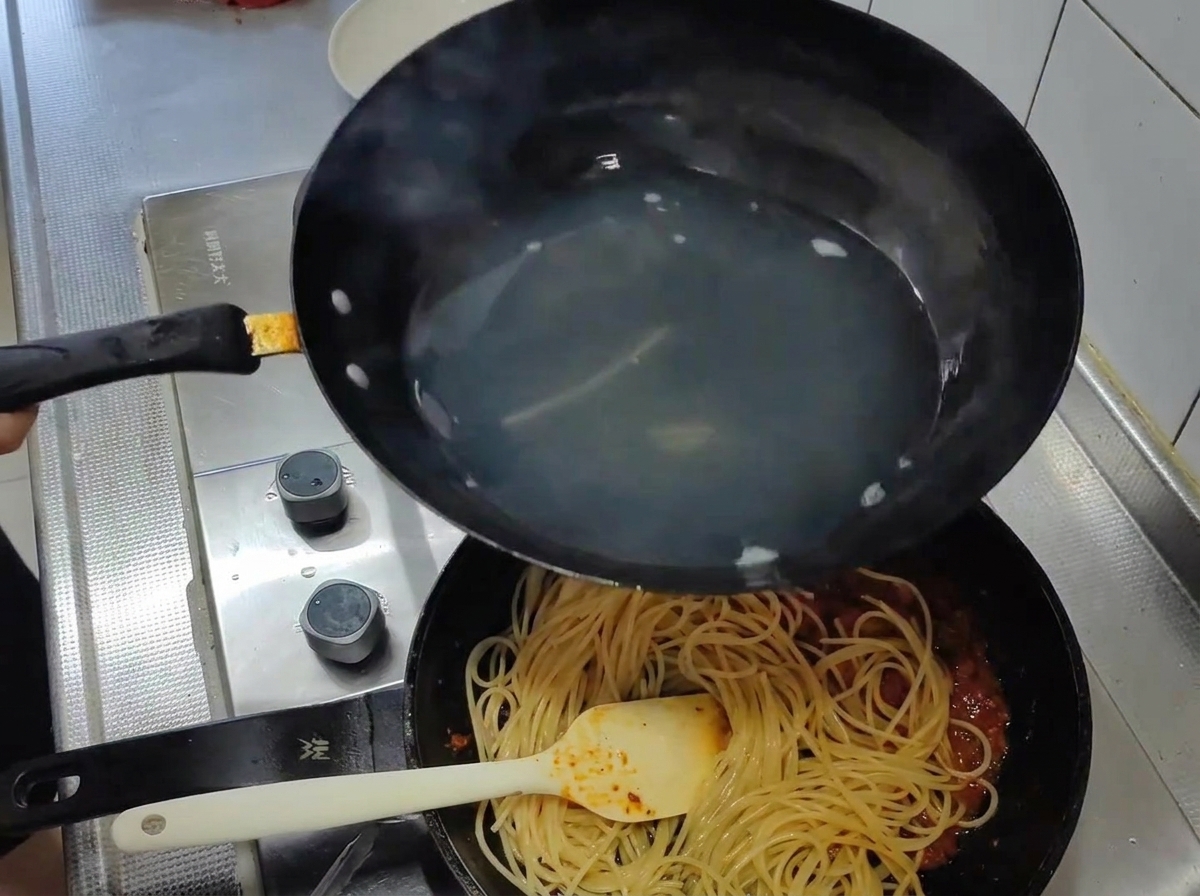 茹で上がったスパゲッティを、沸騰したお湯から直接、濃厚な赤いトマトソースの入ったフライパンに移す様子。