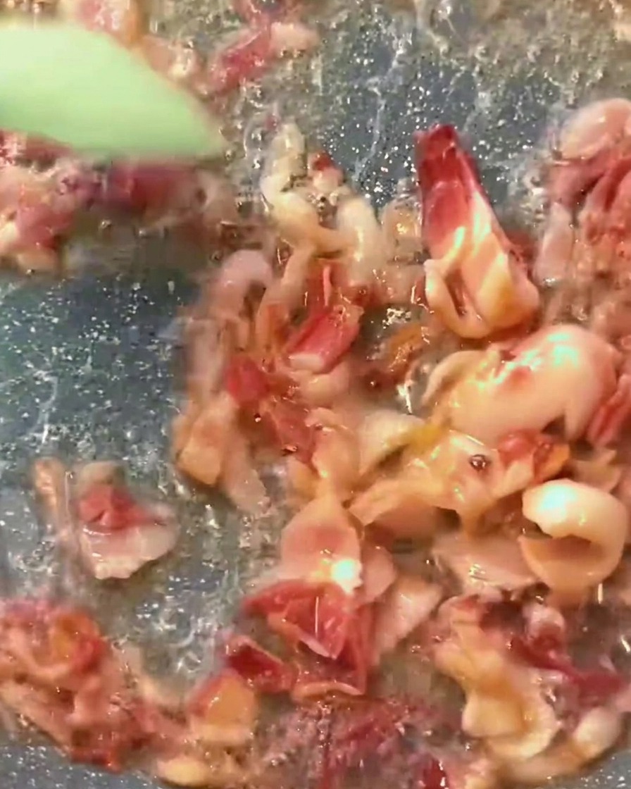 ベーコンの旨味が溶け出した赤いトマトソースがフライパンで煮立っている様子。