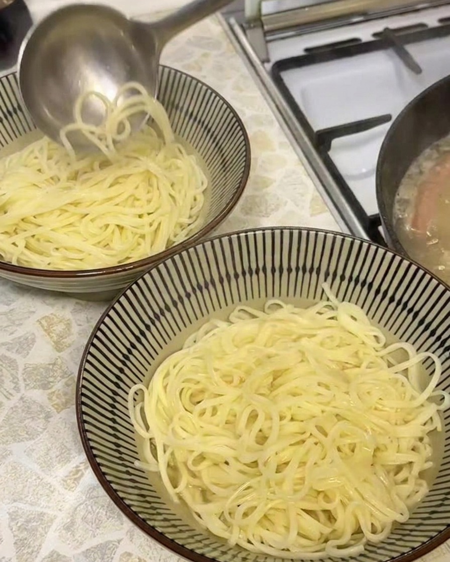 茹でたラーメンの入った丼に、お玉で熱々の黄金色の豚骨風スープを注いでいる様子