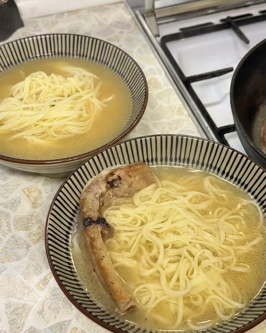 黄金色に輝く柔らかい豚スペアリブを、スープと麺の入った丼に盛り付けている様子