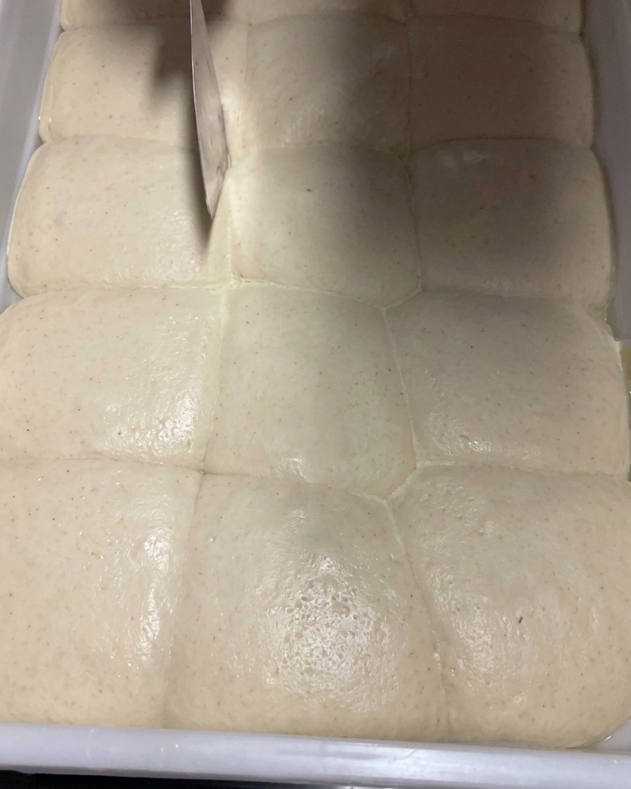 金属製のドゥカッターを使って、発酵したピザ生地を丁寧に分割している様子。