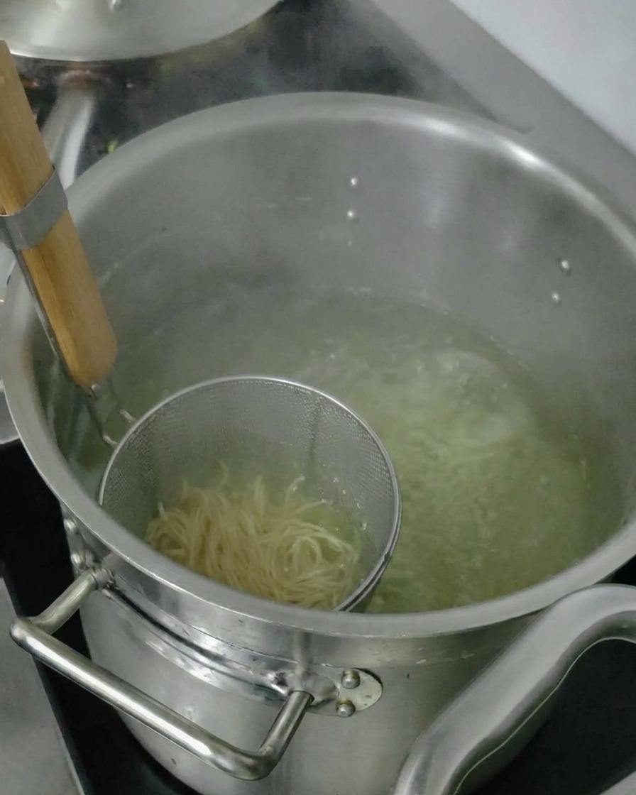 茹で上がった麺をザルで上げ、器に入れる前に水分を切っている様子。