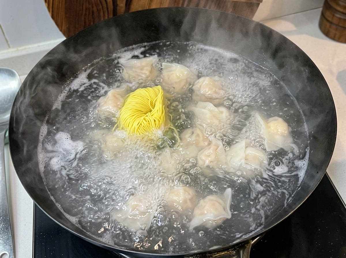 沸騰したお湯の中に、ふっくらとしたワンタンと一緒に束になった黄色い乾燥卵麺を加えている様子。