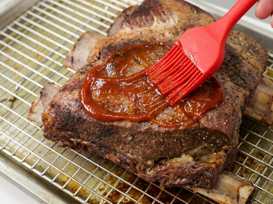網の上の牛リブに、シリコンブラシを使って艶やかなBBQソースをたっぷりと塗っている様子。