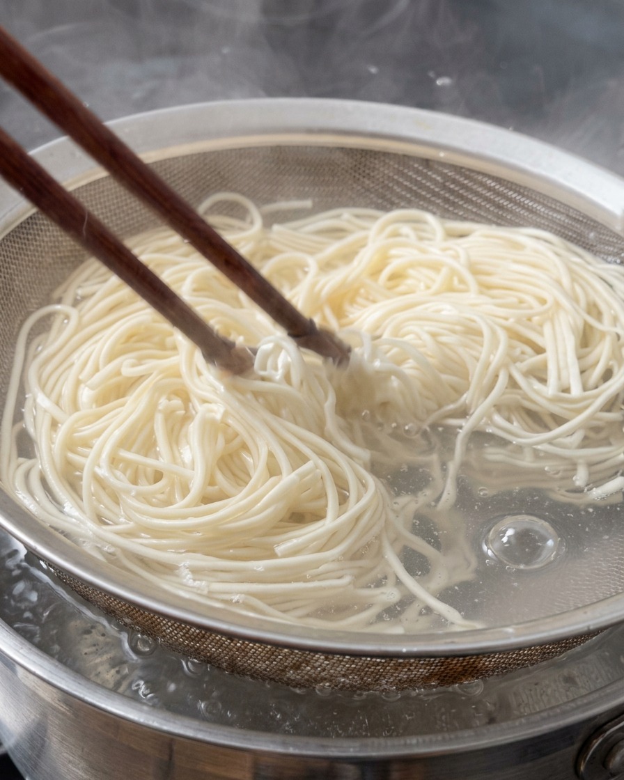箸を使って鍋から茹で上がったラーメンの麺をザルに引き上げている様子。