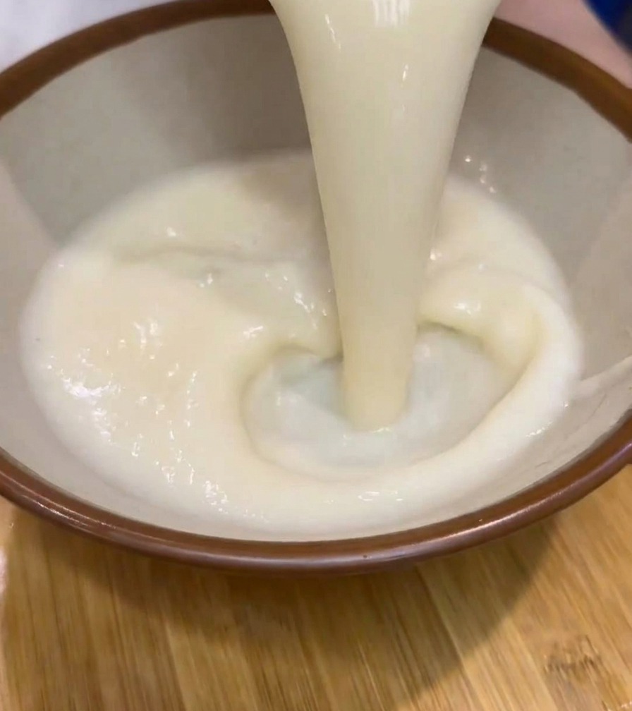 濃厚な白いラーメンスープを、縁が茶色の丼に注いでいる様子。