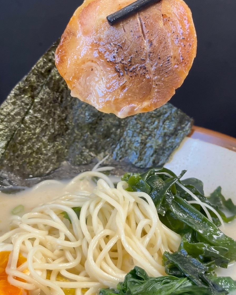 箸でチャーシューを持ち上げ、盛り付けられたラーメンの上に添えようとしている様子。