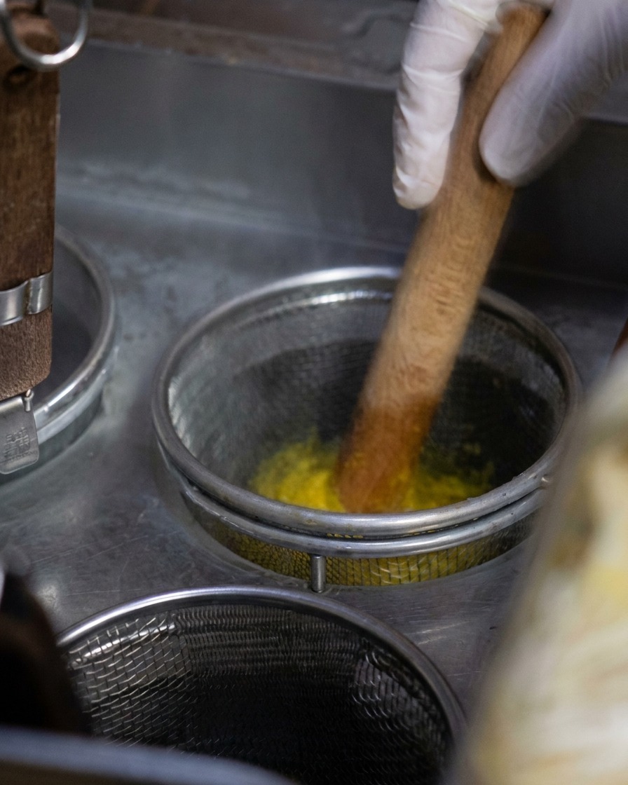 沸騰したお湯の中で黄色い麺を木製の菜箸でかき混ぜている様子。