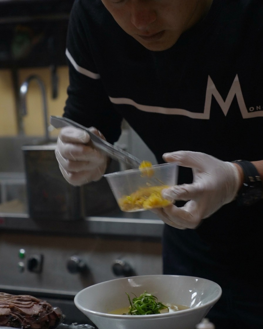 完成したラーメンに、鮮やかな黄色の柚子の皮をスプーンで振りかけている様子。