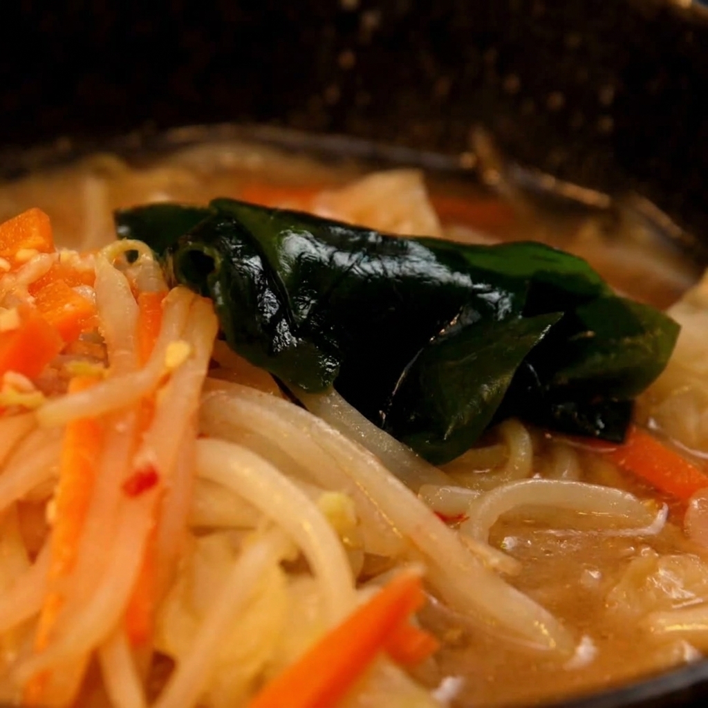 茹で上がった麺を鍋からすくい上げ、用意した味噌スープの入った丼ぶりに移している様子。