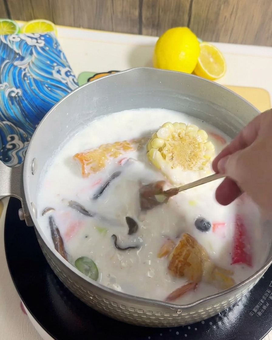 クリーミーなスープと具材が入った鍋に麺を投入している様子。