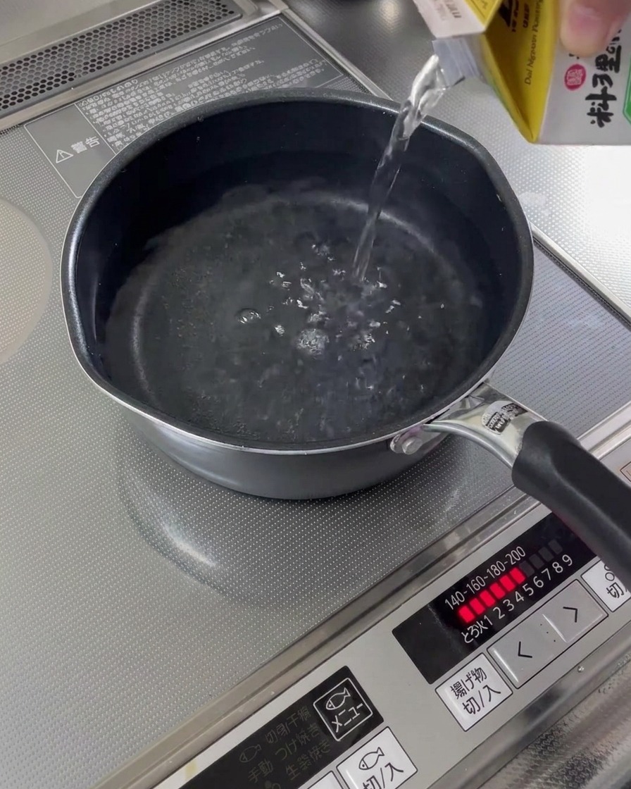 コンロの上の小さな鍋に水が注がれている様子。