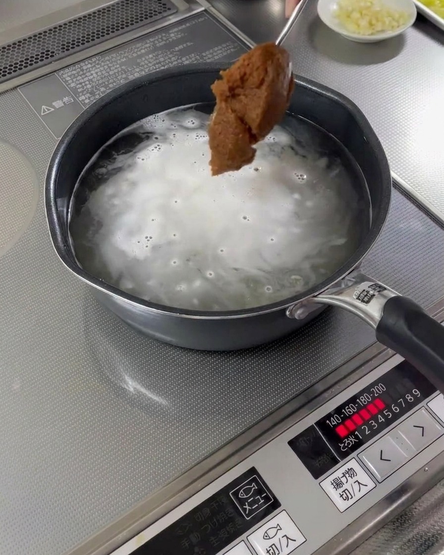 沸騰したスープにスプーン一杯の味噌が加えられている様子。