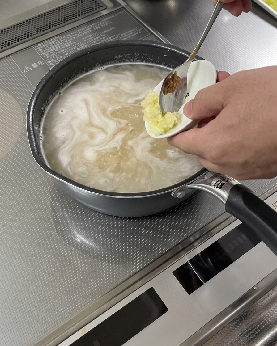 煮立っているスープにおろしにんにくと生姜が加えられている様子。