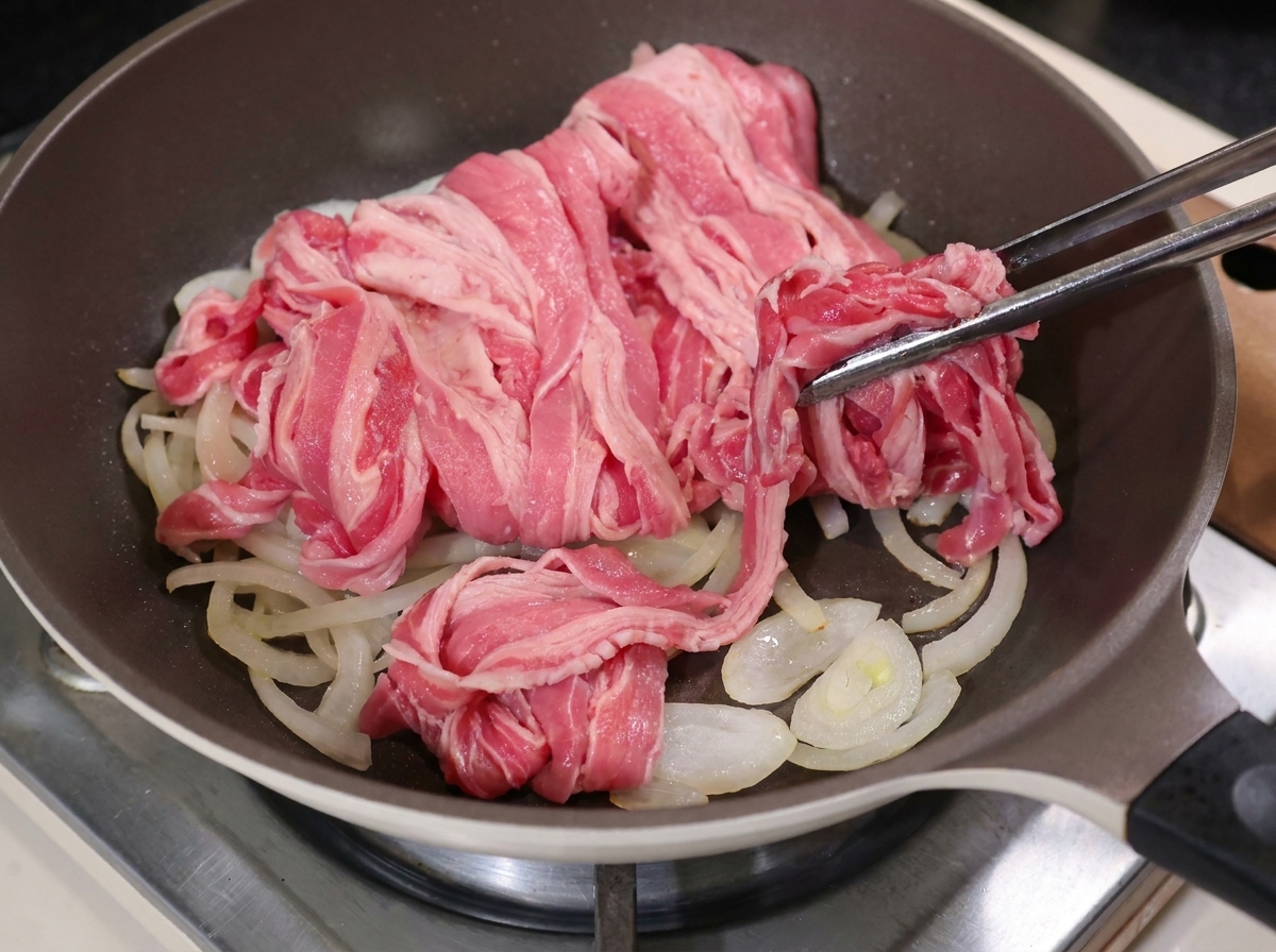 炒めた玉ねぎの上に牛肉を広げている様子