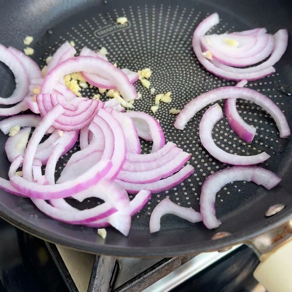 フライパンでバターとともに炒められている玉ねぎとにんにく。