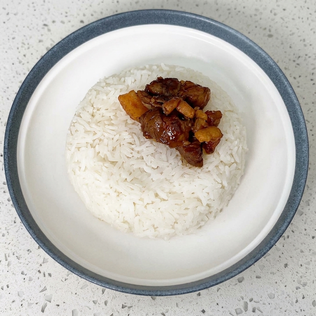 ご飯の上に煮込んだ牛肉を盛り付けている様子。