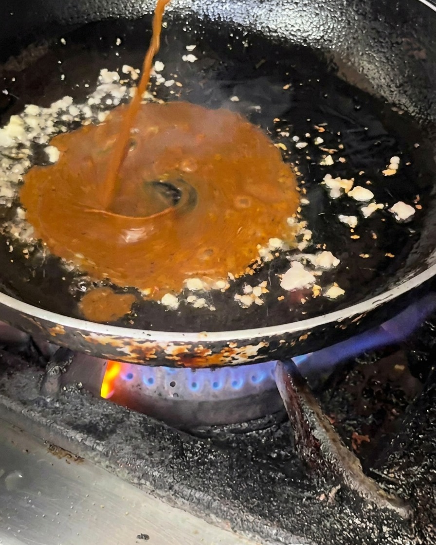 炒めた薬味が入ったフライパンに、黒胡椒ソースと照り焼きソースを注ぎ入れている様子。