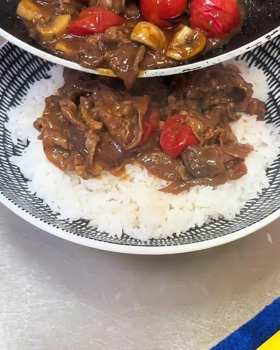 ご飯の上に、炒めた牛肉とマッシュルームを盛り付けている様子。