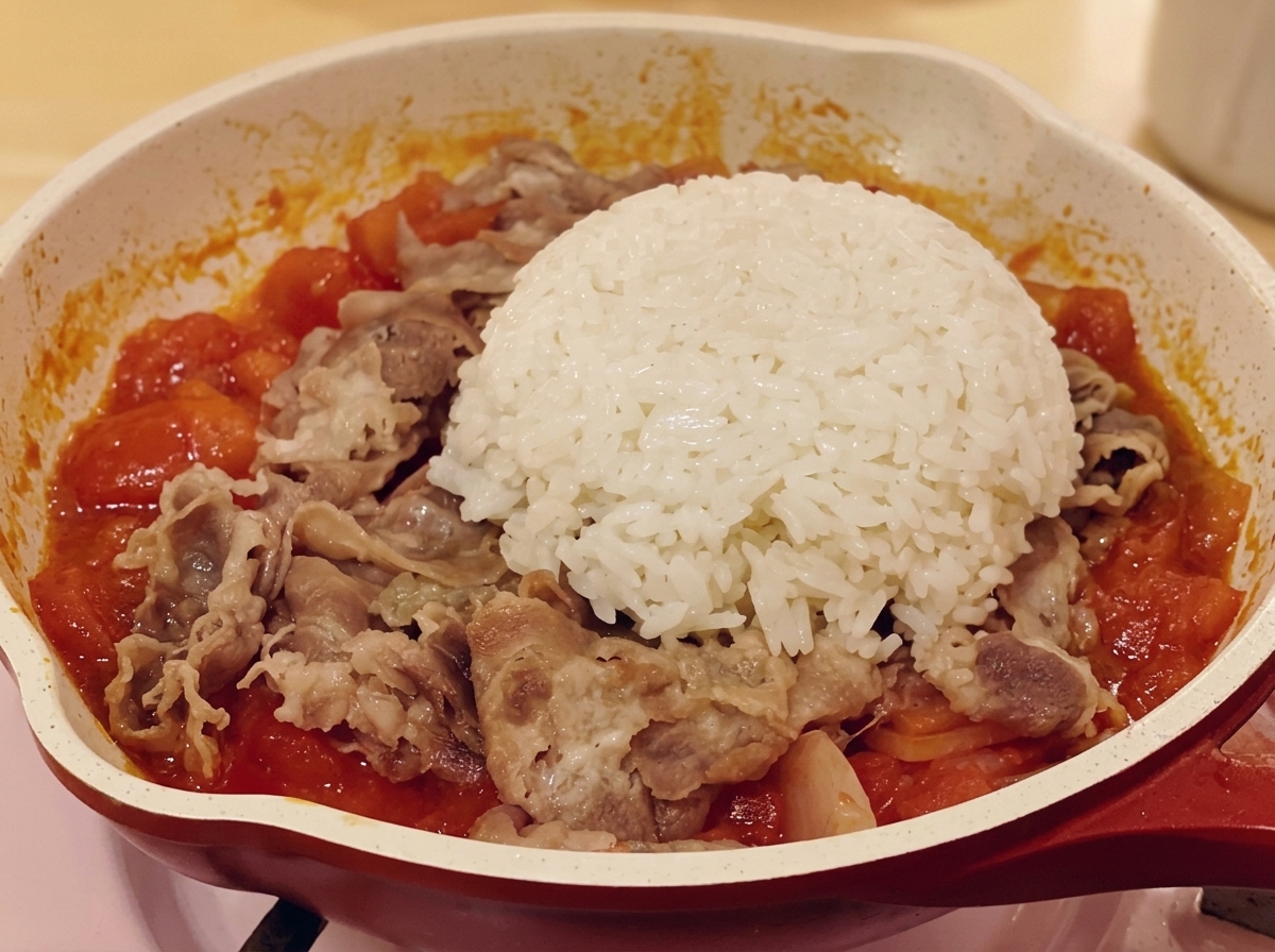 牛肉とトマトの具材の上に炊いたごはんをのせている様子。